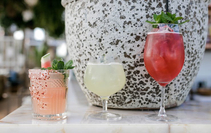 three cocktails sitting on a bench in front of a pot.