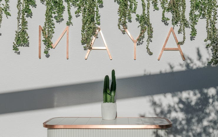 A gold sign saying Maya on a white wall.