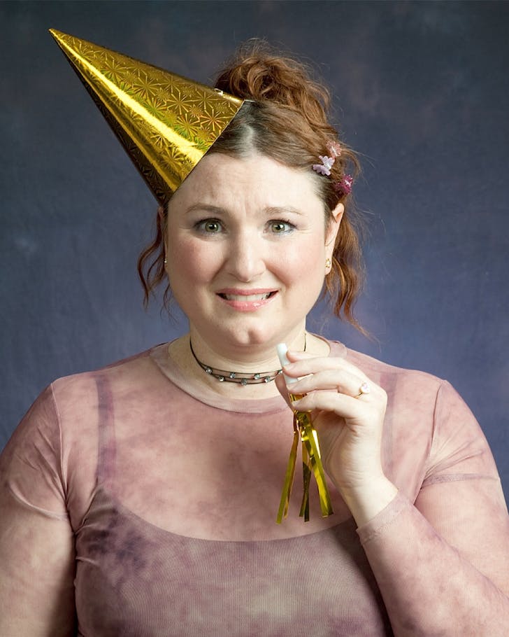 A woman wearing a 90s-inspired outfit and a gold party hat. 