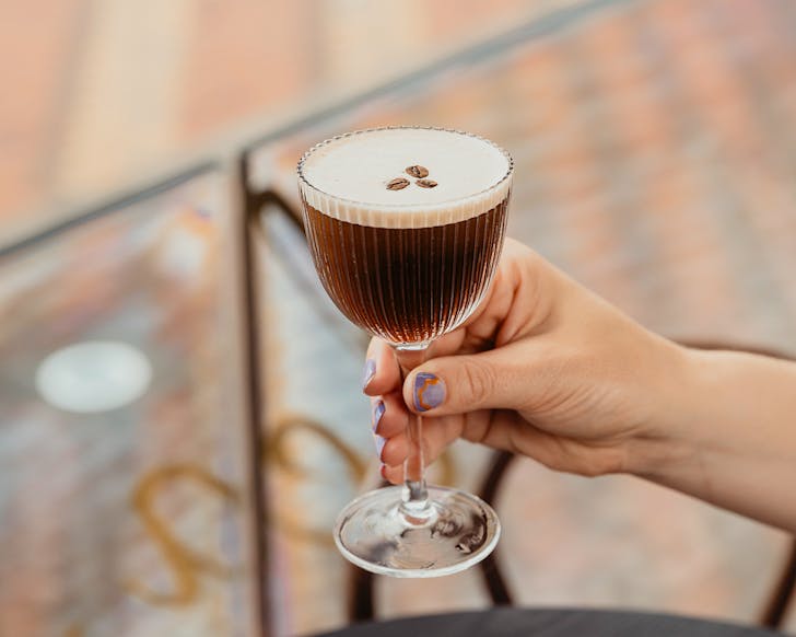 Someone with pretty purple nails holds an espresso martini. 