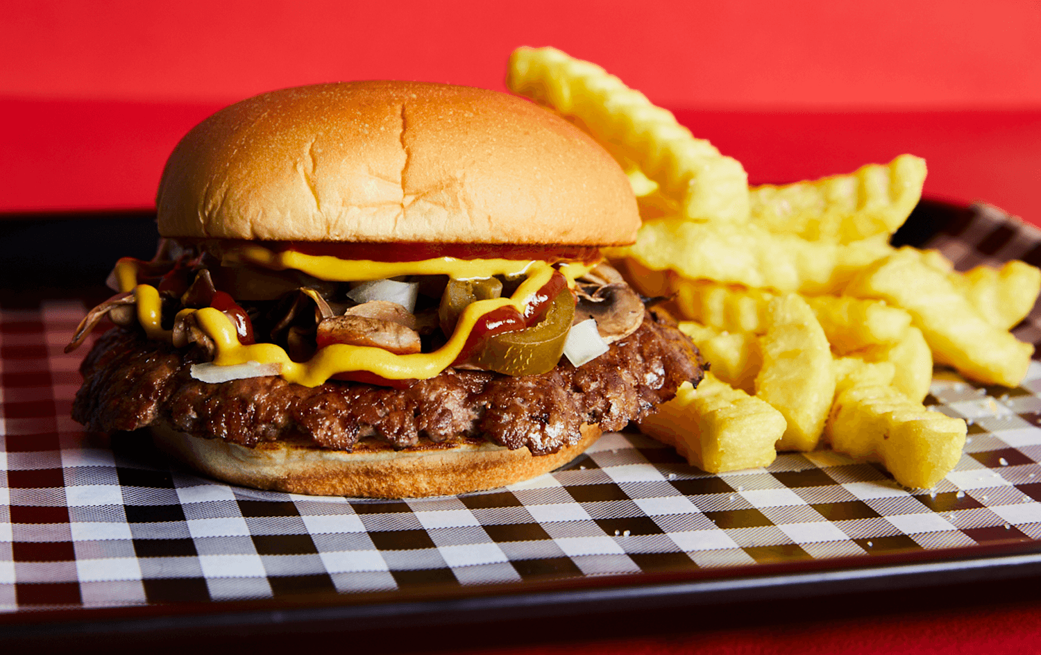 A juicy burger sitting atop tartan printed paper. Pickles hang out the side of one of Melbourne's best burgers.