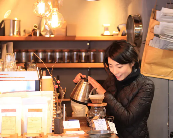 A roaster pours drip coffee in the warmly lit Mel Coffee Roasters shop in Osaka.