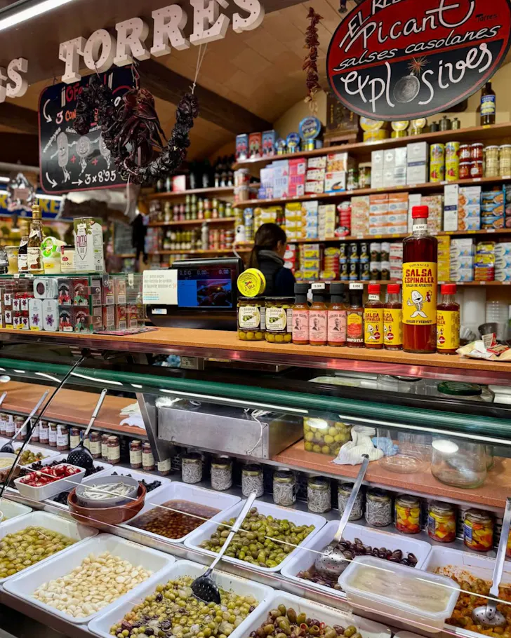 A vibrant stall at Mercat De Santa Caterina in Barcelona, selling olives, salsa and spices.