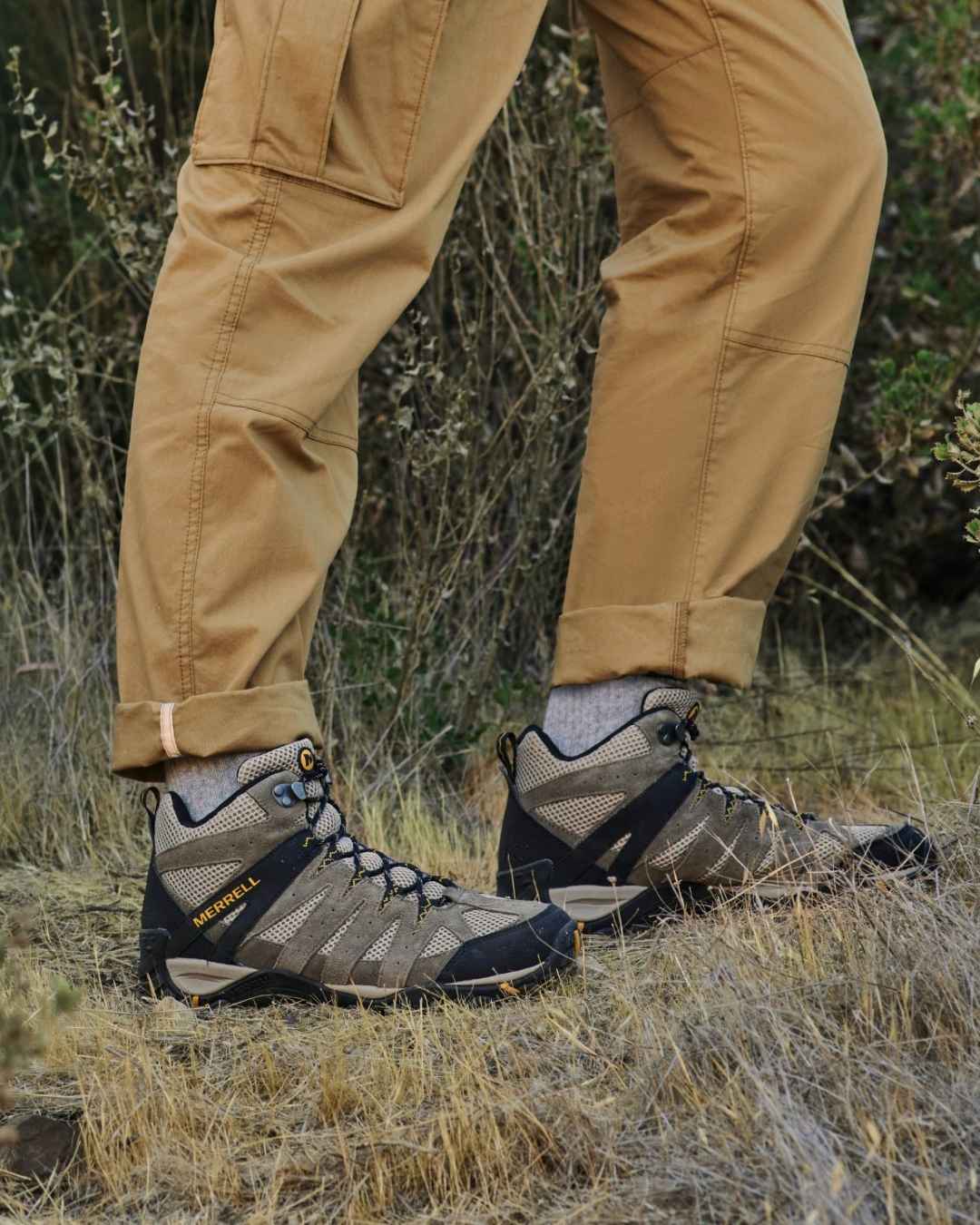 A person's legs from the thighs down wearing camel coloured hiking pants and shoes