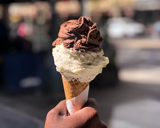A hand holding a cone topped with chocolate and hazelnut gelato