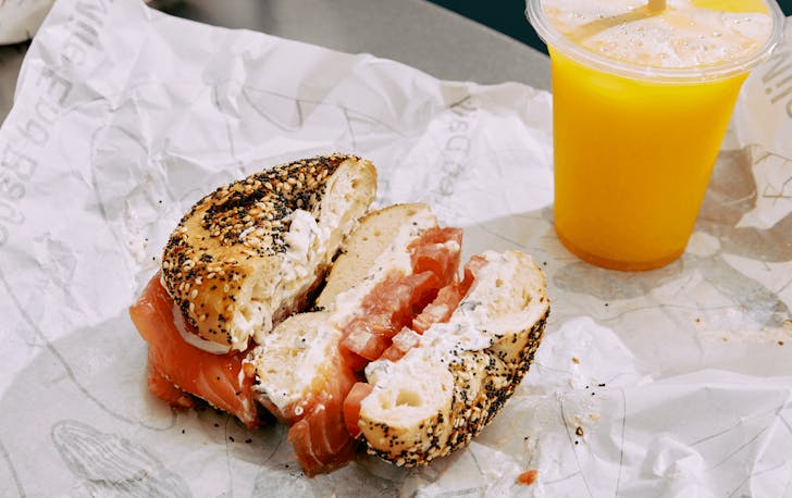 A thick salmon and tomato bagel with an orange juice, a best bagel Melbourne option.