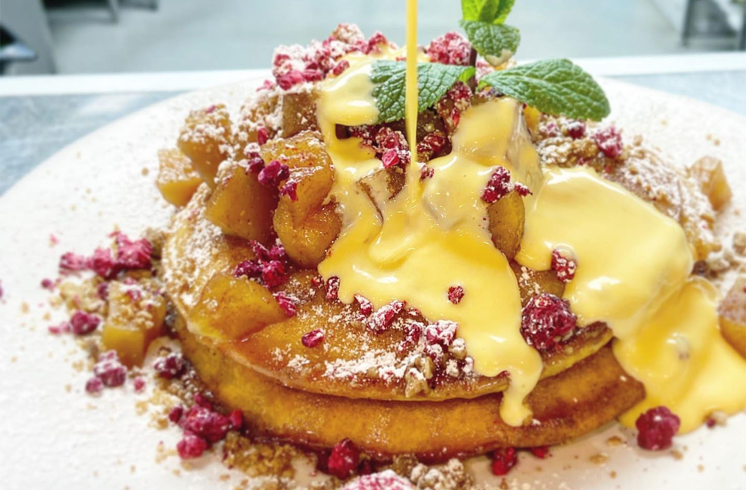 Plate of apple crumble pancakes poured over with anglaise sauce at Milk And Honey, one of the best cafes in Hawke's Bay.