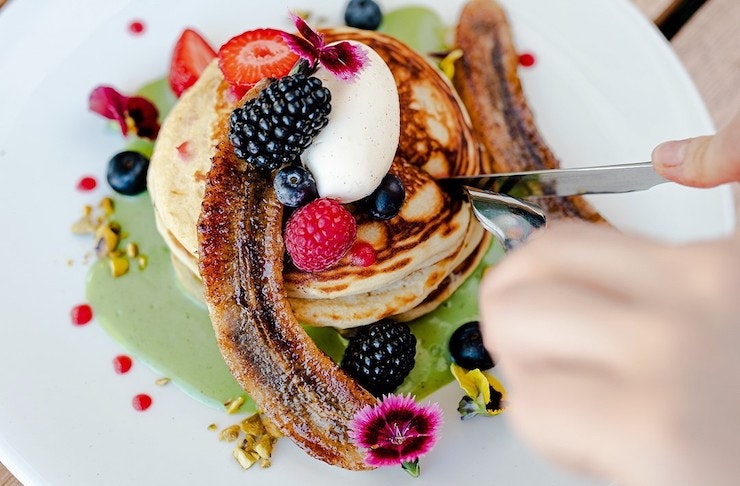 hands cutting into a stack of pancakes