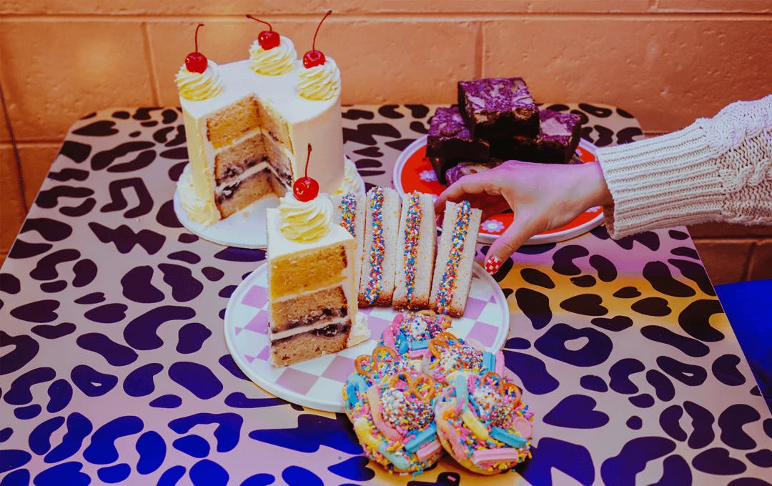 A hand reaching over at a table of desserts. 