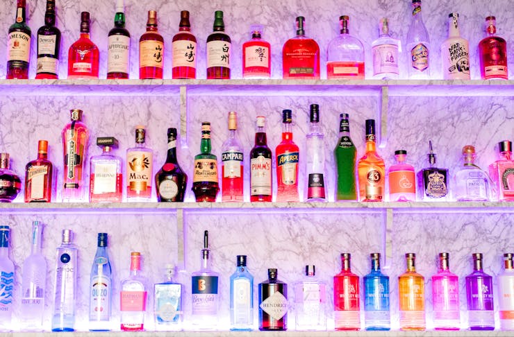 Three bar shelves are lined with many liquor bottles.