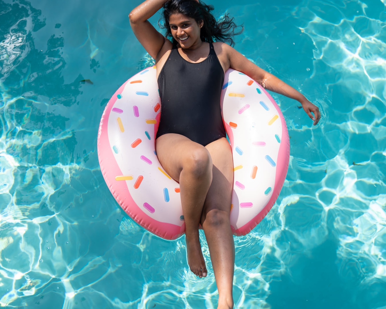 A woman in a black one piece relaxes on a blow up doughnut in a pool.