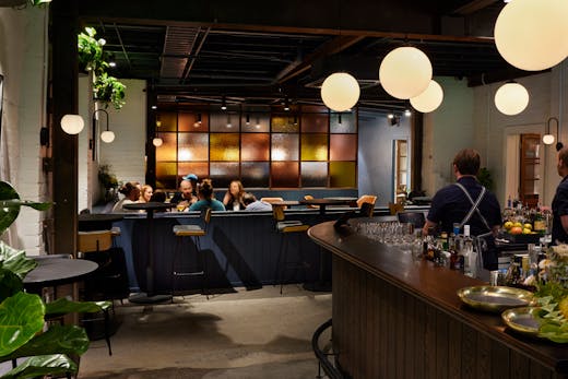 The inside of a bar with plants and pendant lights.