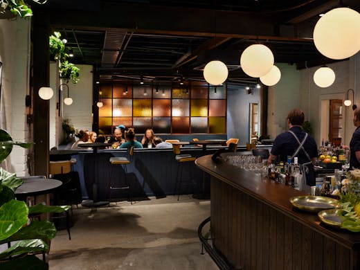The inside of a bar with plants and pendant lights. 