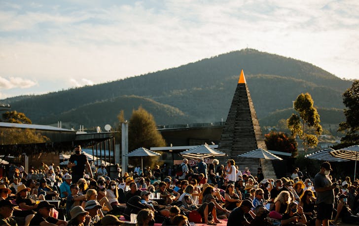 A crowd lying in the sun with a large green hill in the background.