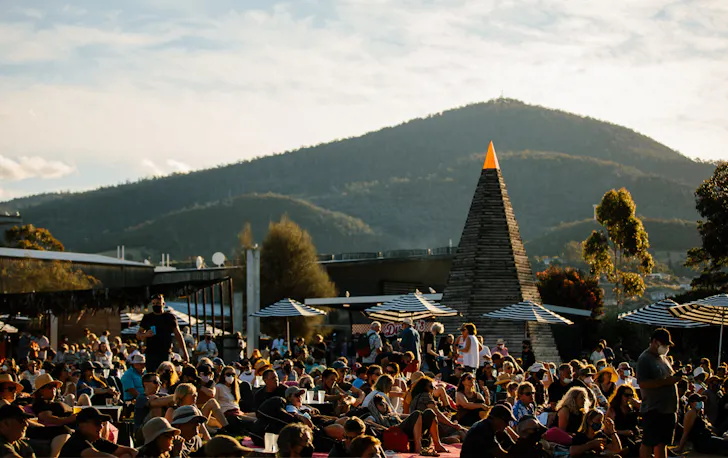 A crowd lying in the sun with a large green hill in the background.