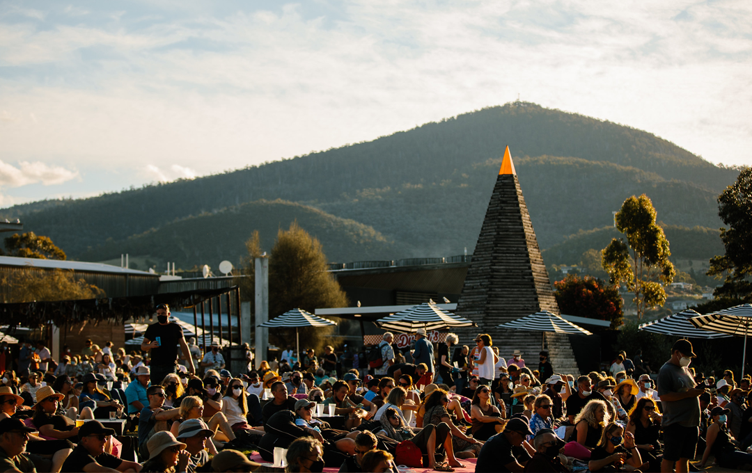 A crowd lying in the sun with a large green hill in the background.