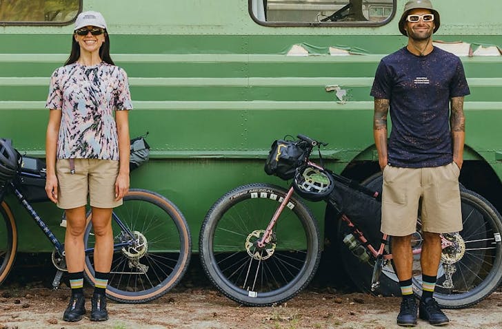 Two people stand in front of a green campervan with bikes and clad in Mons Royale. 