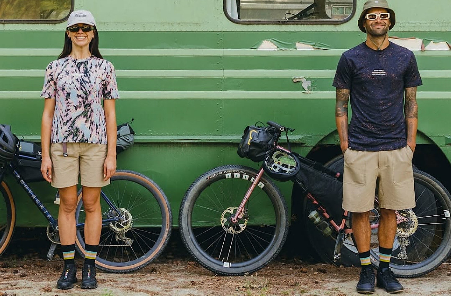 Two people stand in front of a green campervan with bikes and clad in Mons Royale. 