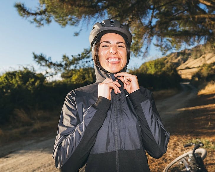 A woman zips up a shell jacket and pokes her tongue out at the camera. 