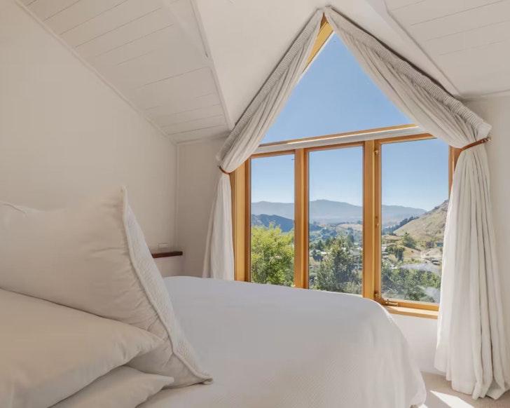 A view of the mountains through the picture window in the bedroom at Moonlight Cottage romantic stay in Queenstown, New Zealand