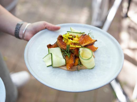 A hand holding a plate of roast pumpkin and thin slices of zucchini.