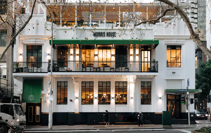 A white pub on a corner with lights on inside. 