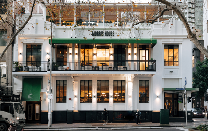A white pub on a corner with lights on inside. 