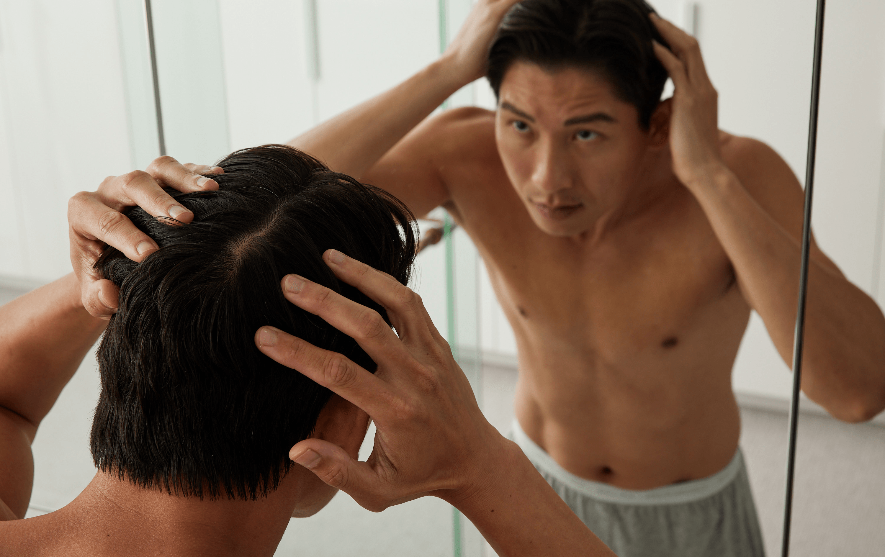 A man looking in a mirror at his hair. 