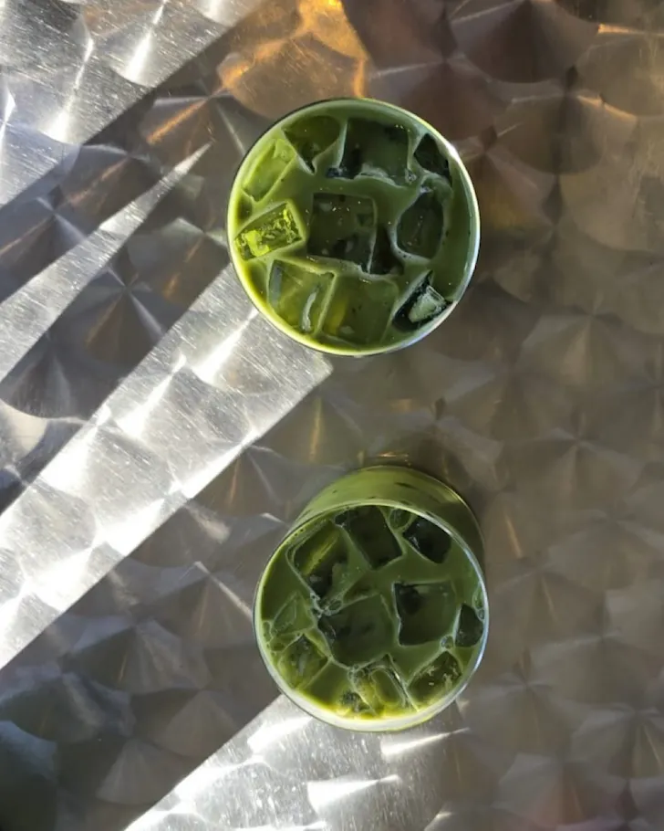 Two glasses of matcha on a silver table. 