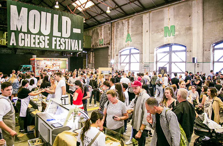 The inside of the cheese festival with people tasting cheese and a green banner that reads Mould Cheese Festival