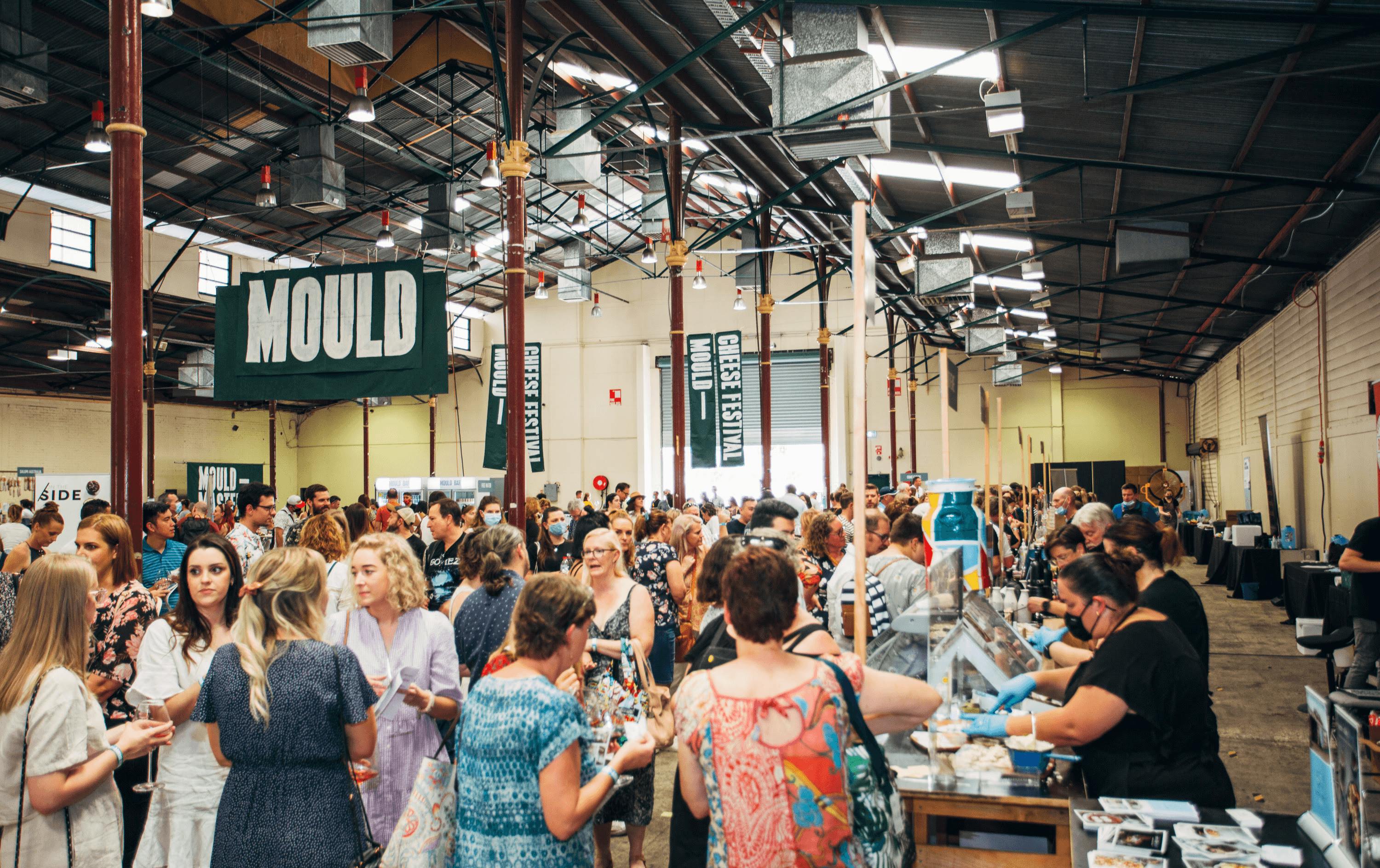 A busy hall filled with people and cheese stands.