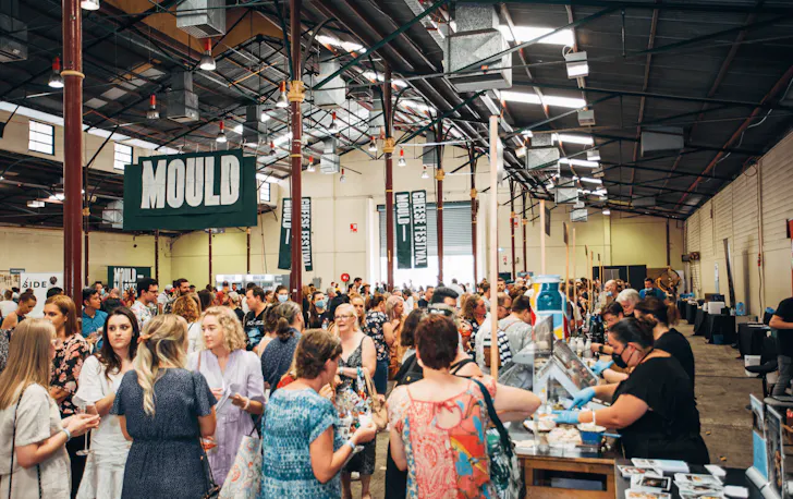 A busy hall filled with people and cheese stands.