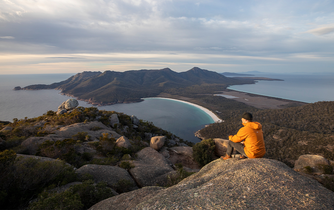 a person sitting on a rock overlooking a sandy bay and mountains 
