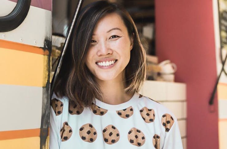 Deanna Yang of Moustache Milk and Cookie Bar stands in front of her cookie bus. She is also wearing a shirt with cookies on it.