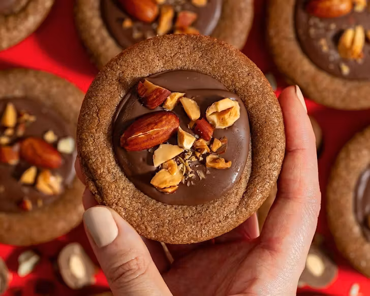 Someone with neutral-toned fingernails holds up a scorched almond cookie pie. 