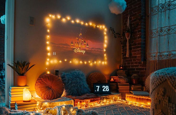 An at home-cinema with projected screen surrounded by fairy lights and cushions