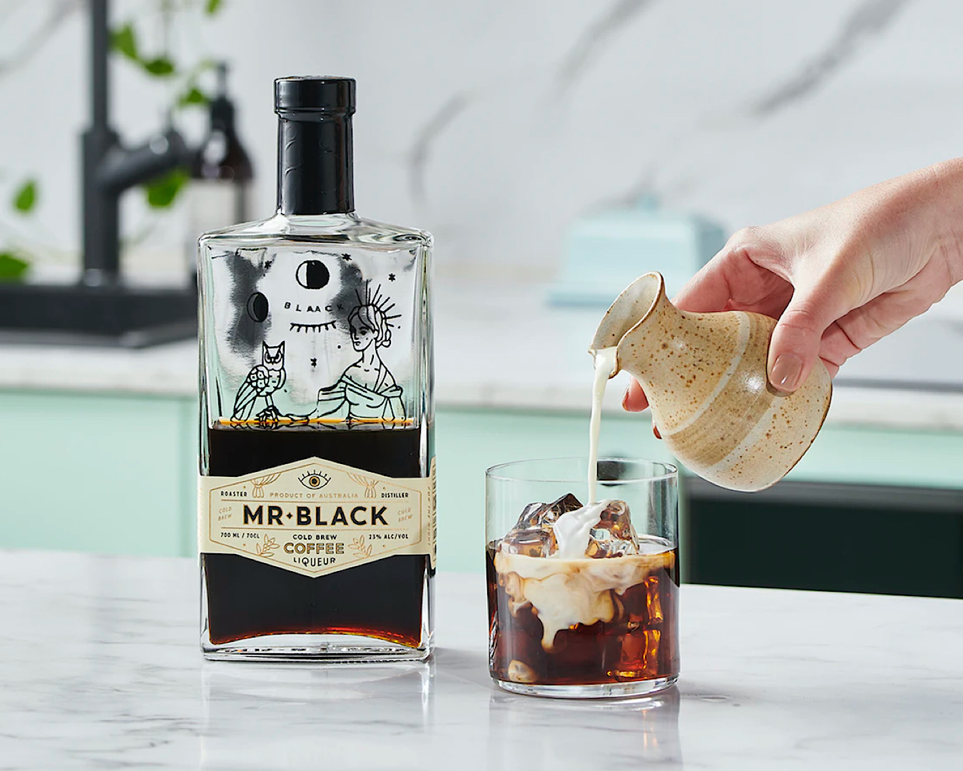 Somebody pours cream into a glass of ice, vodka and coffee liqueur. Next to the glass is a half full bottle of Mr Black coffee liqueur. 
