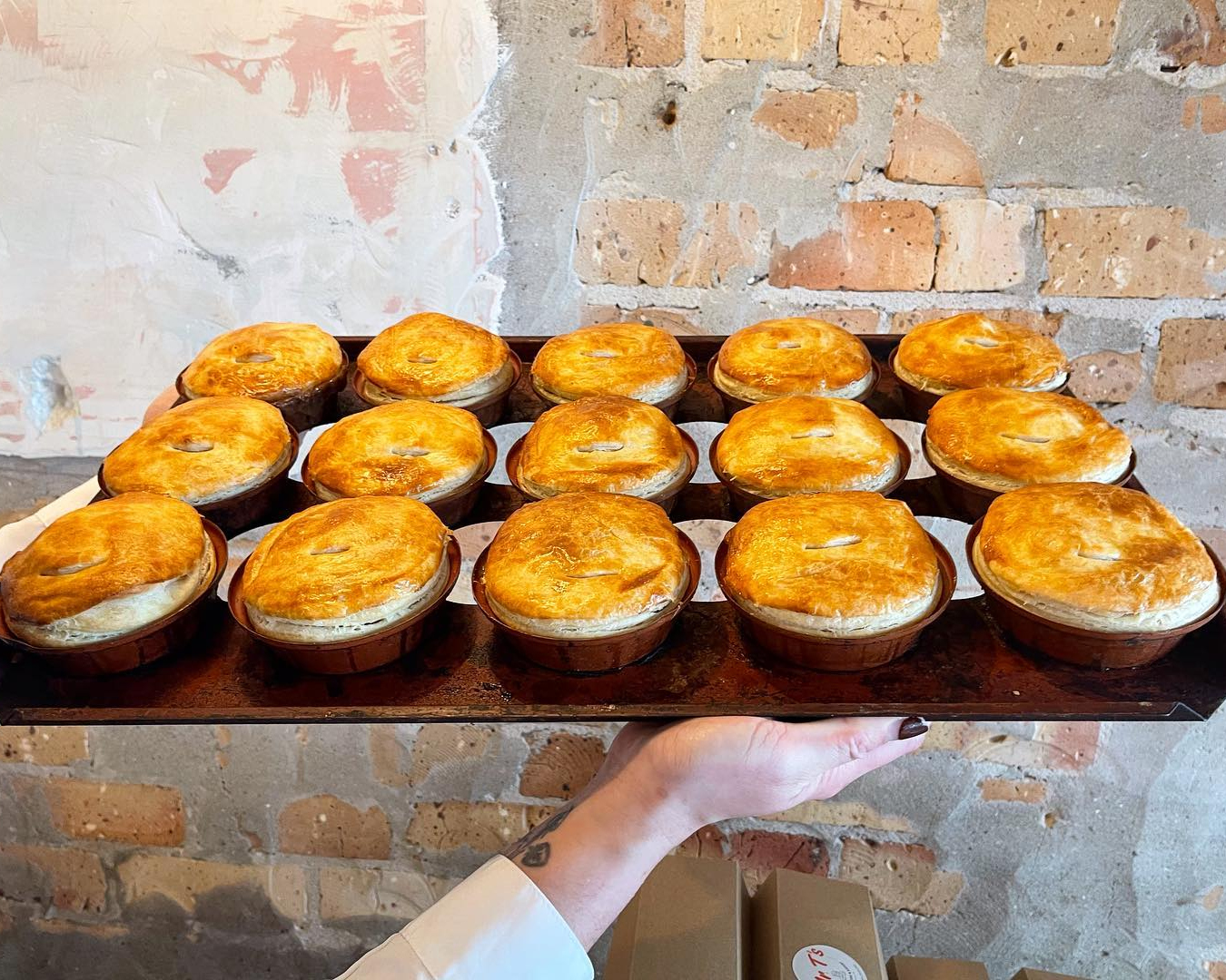 A person holds a tray of 15 perfectly golden pies. 