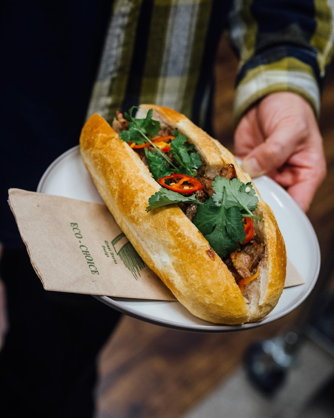 A person holds a plate bearing a delicious-looking bánh mì roll. 