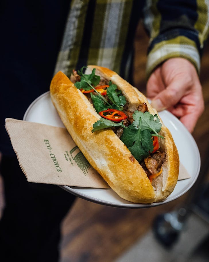 A person holds a plate bearing a delicious-looking bÃ¡nh mÃ¬ roll. 