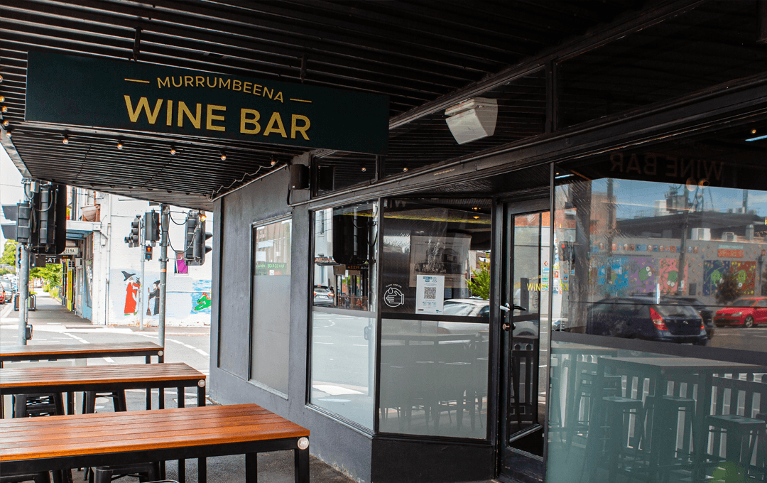 The out front of a bar with tables and a green sign. 
