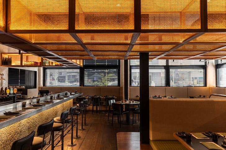 The interior of New Quarter with no diners, a concrete bar and floor and a wicker shelving feature thats lit up.