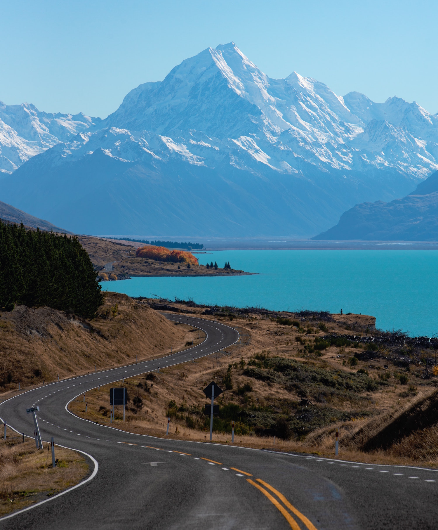 A road snakes it way down to Lake Pukaki with snowcapped mountains in the distance.