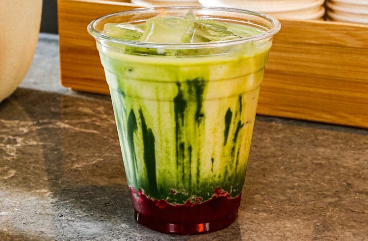 A matcha latte with raspberry puree at the bottom of the cup sitting on a bench.