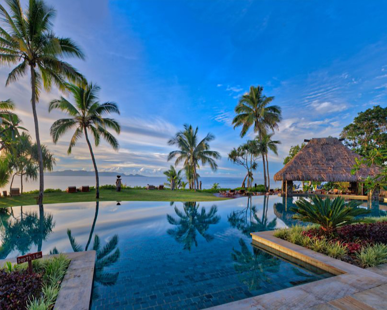 Nanuku Resort Fiji’s jaw-droppingly stunning clubhouse pool with palm tree reflections and a direct view of the ocean. 