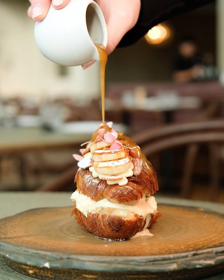 Someone pours banana rum caramel over a croissant at Origine. 
