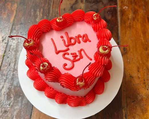A pink and red retro heart-shaped cake decorated with cherries and the words 'Libra szn.'