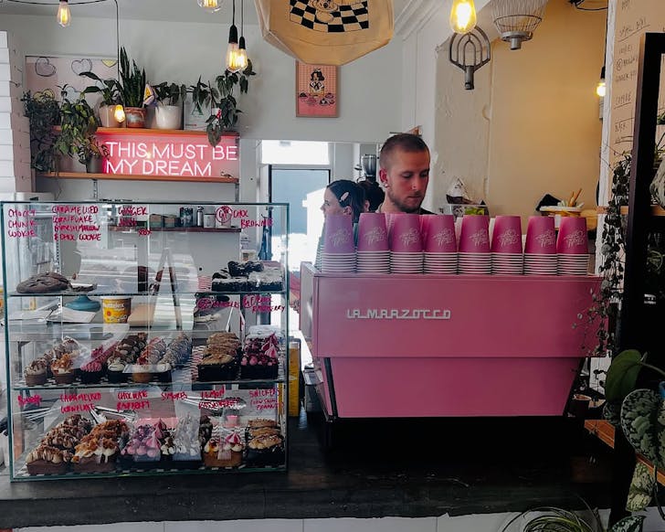 A pretty pink coffee machine and a cabinet filled with teeny tiny plant-based treats at Neat Cakes. 