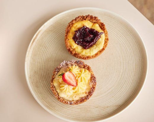 A plate with a small lemon cheesecake and blackberry cheesecake