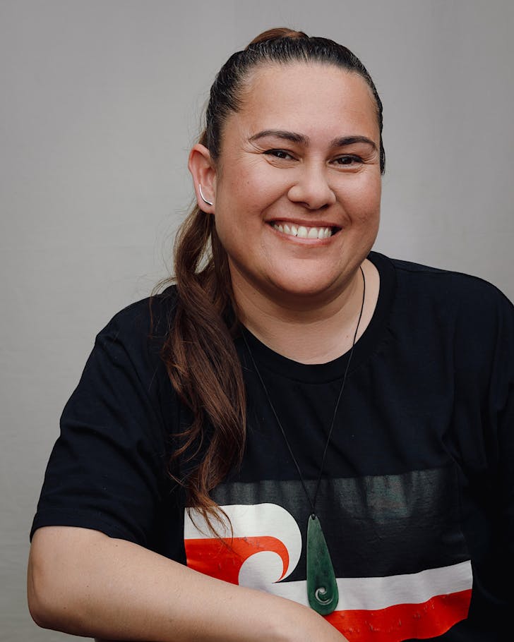 Nicole Horan wears a pounamu necklace and a black t-shirt with the Tino Rangitiratanga flag on it, and smiles. 